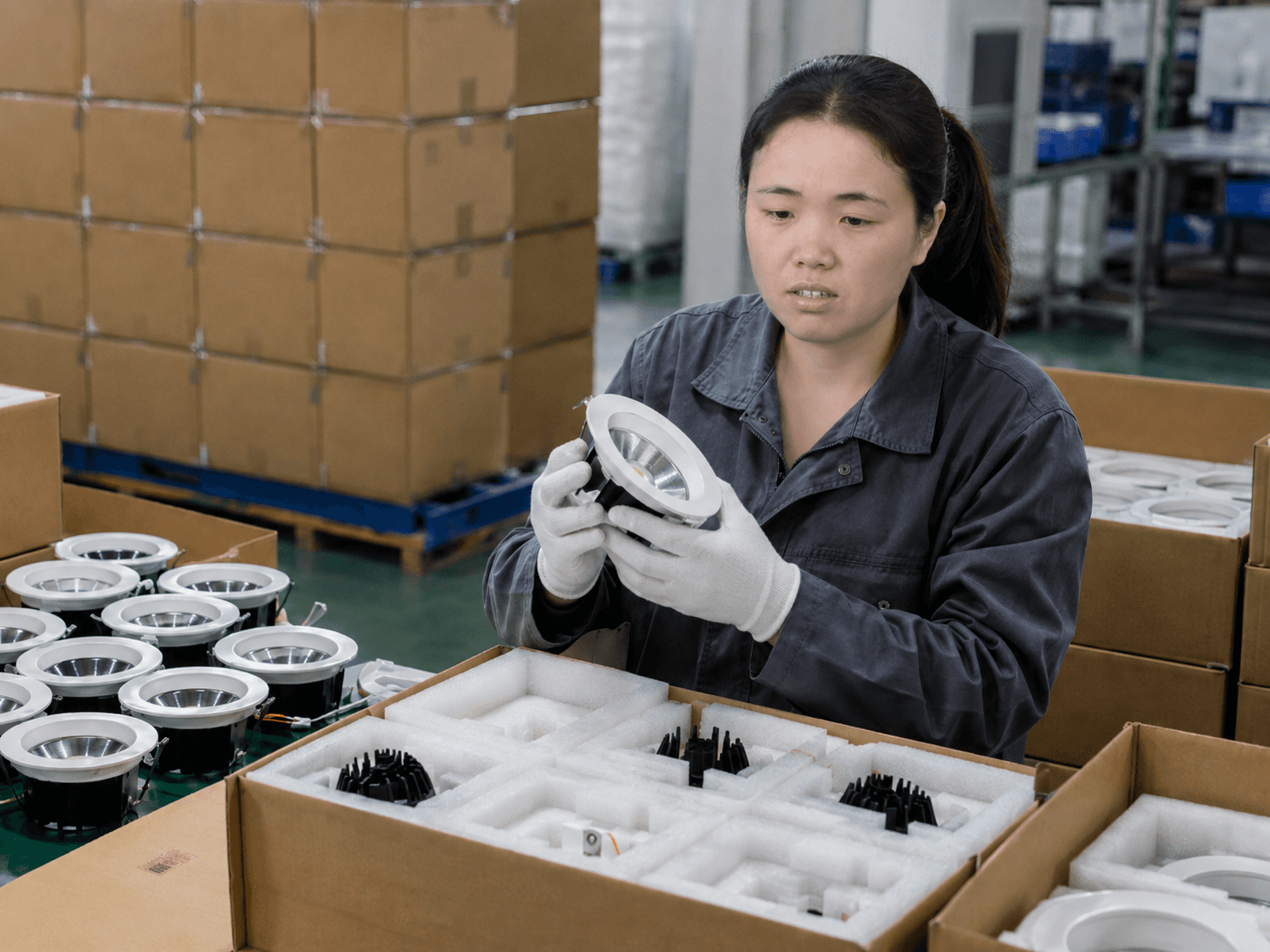 Factory technician inspecting finished LED downlights beside protective shipment packaging